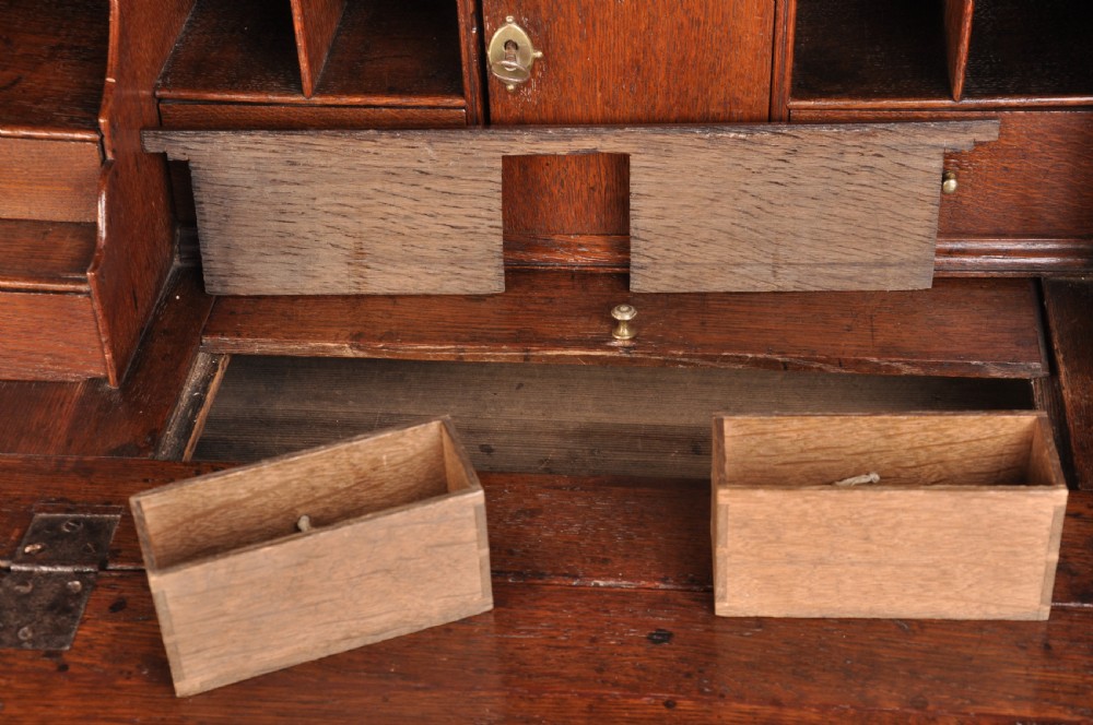 An early eighteenth-century oak bureau featuring a slanted drop-front desk above graduated drawers with brass drop handles and bracket feet. View X