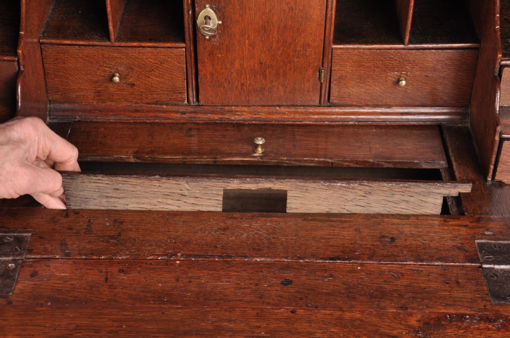 An early eighteenth-century oak bureau featuring a slanted drop-front desk above graduated drawers with brass drop handles and bracket feet. View XI