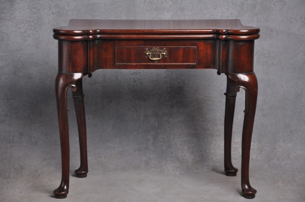 An 18th-century mahogany fold-over card table featuring slender cabriole legs, pad feet, a central drawer with a brass swing handle, and shaped corners.