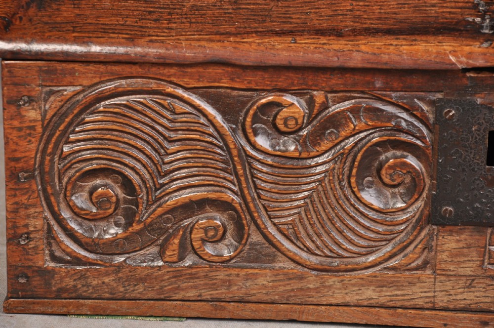 A 17th-century carved oak desk box featuring a sloped writing lid, iron hinges, iron lock plate, and hand-carved scroll motifs across the front panel. View III