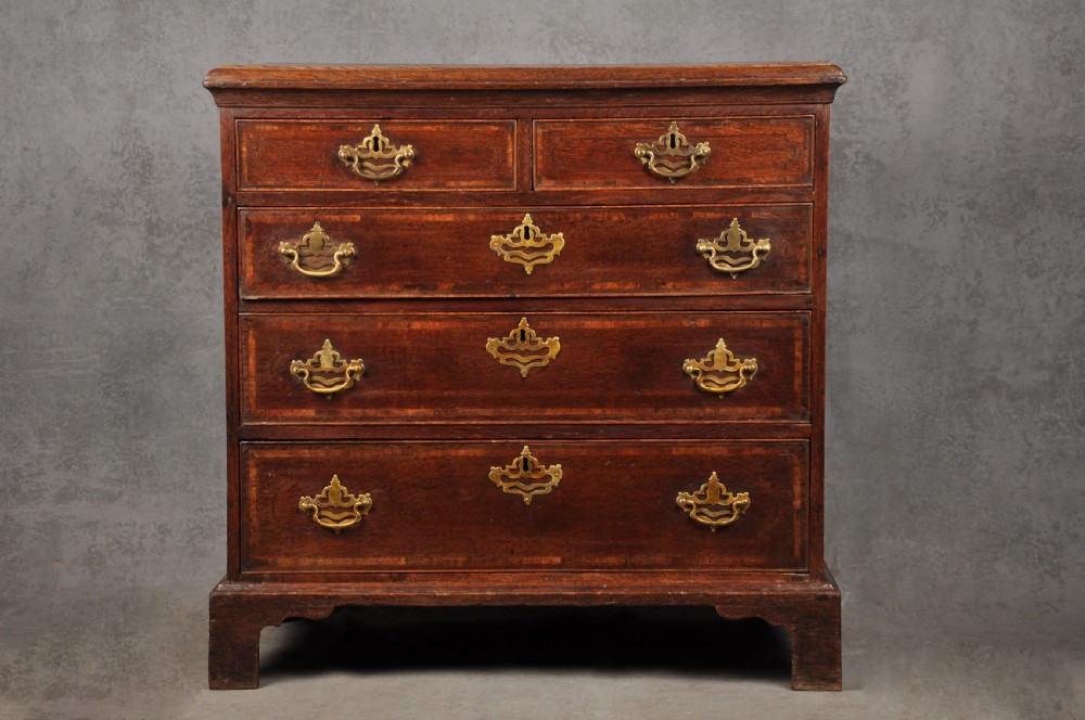 An 18th-century dark oak chest of drawers featuring inlaid drawer borders, pierced brass handles, keyhole escutcheons, and bracket feet.
