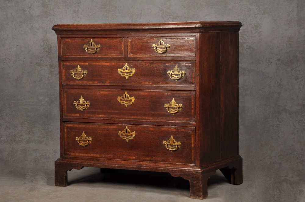 An 18th-century dark oak chest of drawers featuring inlaid drawer borders, pierced brass handles, keyhole escutcheons, and bracket feet. View II