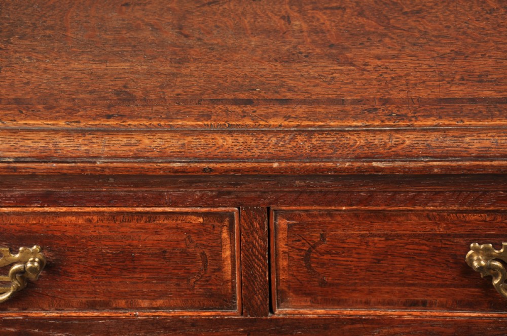 An 18th-century dark oak chest of drawers featuring inlaid drawer borders, pierced brass handles, keyhole escutcheons, and bracket feet. View V