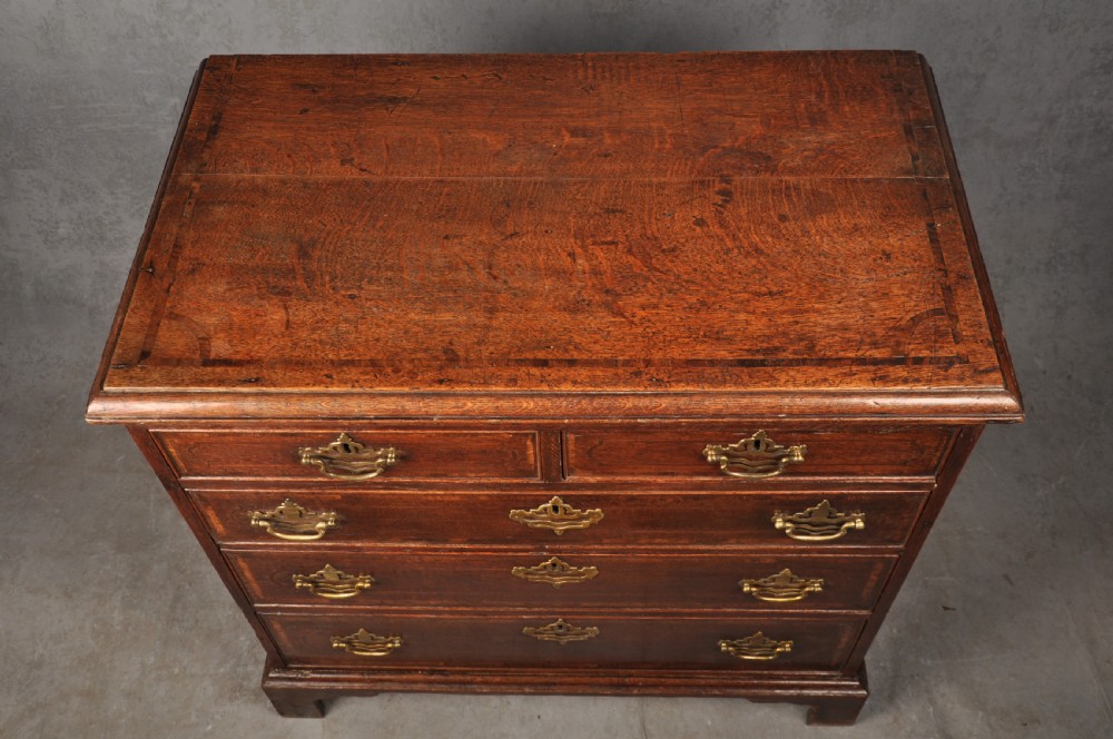 An 18th-century dark oak chest of drawers featuring inlaid drawer borders, pierced brass handles, keyhole escutcheons, and bracket feet. View VI