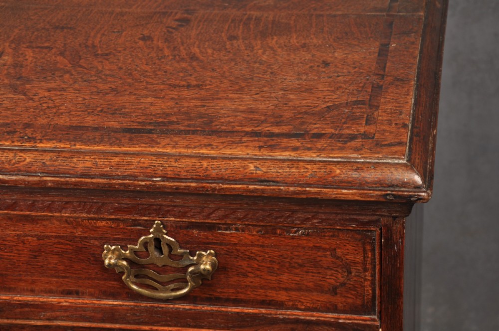 An 18th-century dark oak chest of drawers featuring inlaid drawer borders, pierced brass handles, keyhole escutcheons, and bracket feet. View VII