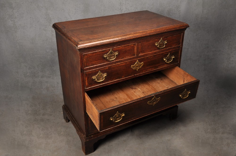 An 18th-century dark oak chest of drawers featuring inlaid drawer borders, pierced brass handles, keyhole escutcheons, and bracket feet. View VIII