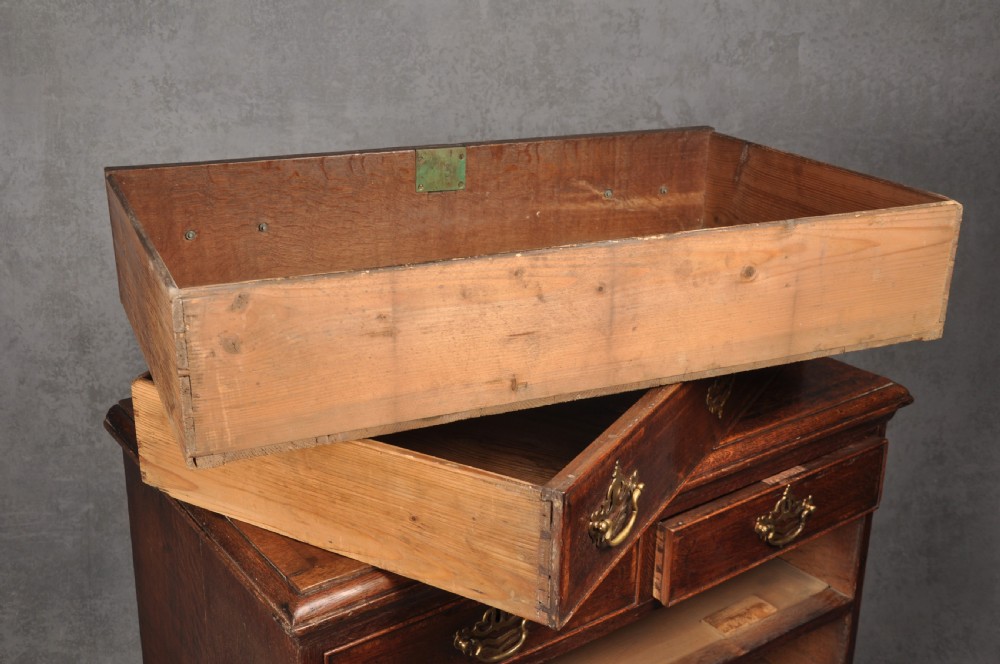 An 18th-century dark oak chest of drawers featuring inlaid drawer borders, pierced brass handles, keyhole escutcheons, and bracket feet. View IX