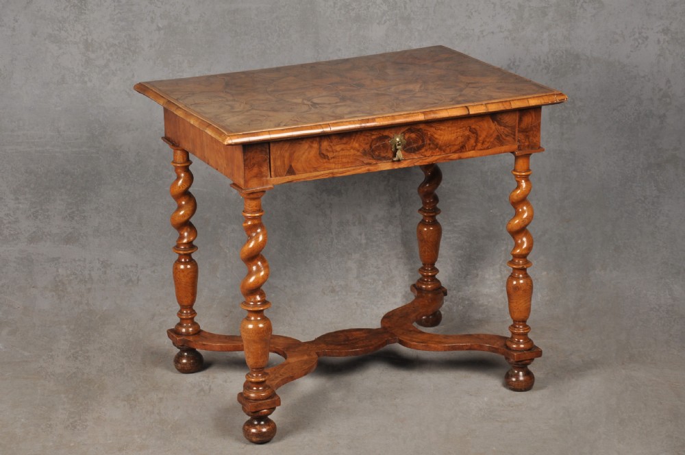 An antique olive wood side table featuring geometric oyster veneering on top, a single drawer with a brass drop handle, four barley twist legs, and a curved stretcher base.