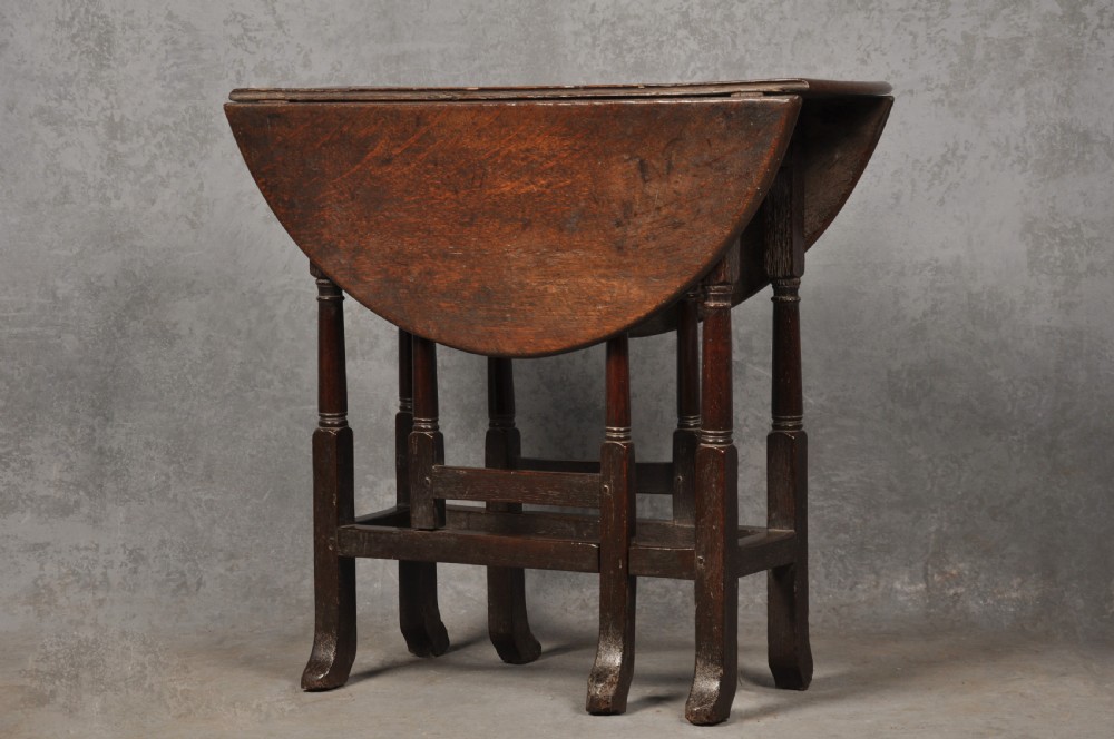 A small dark brown Queen Anne oak gateleg table shown with both drop leaves lowered, featuring turned legs and a stretcher base.
