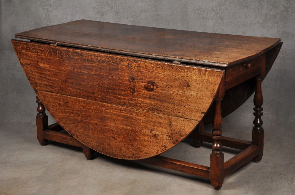A large 17th-century solid oak gateleg dining table with two drop leaves, turned legs, and square box stretchers.