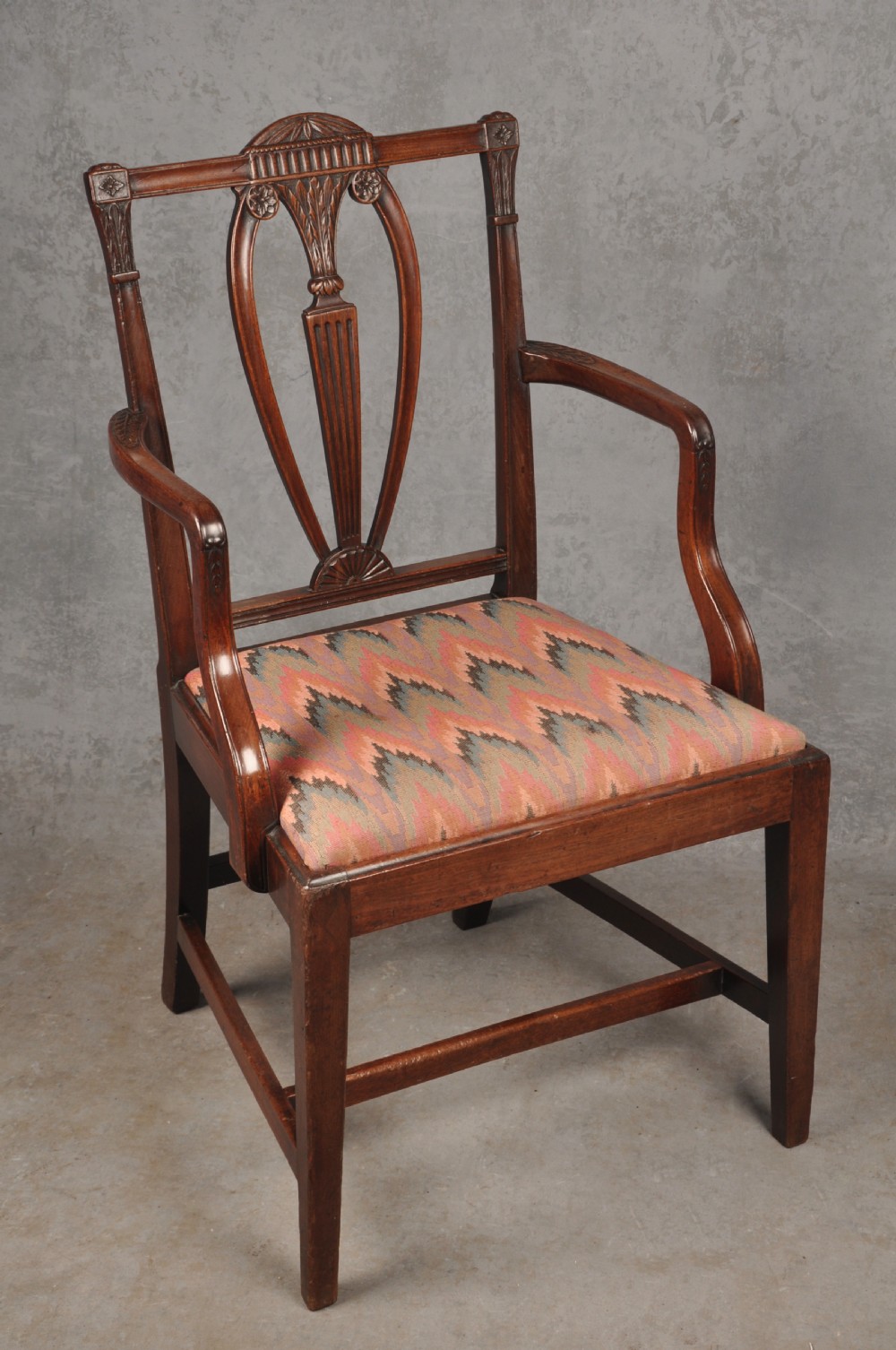 An 18th-century dark mahogany open armchair with a carved back splat, curved arms, square legs with stretchers, and pattern-upholstered seat.
