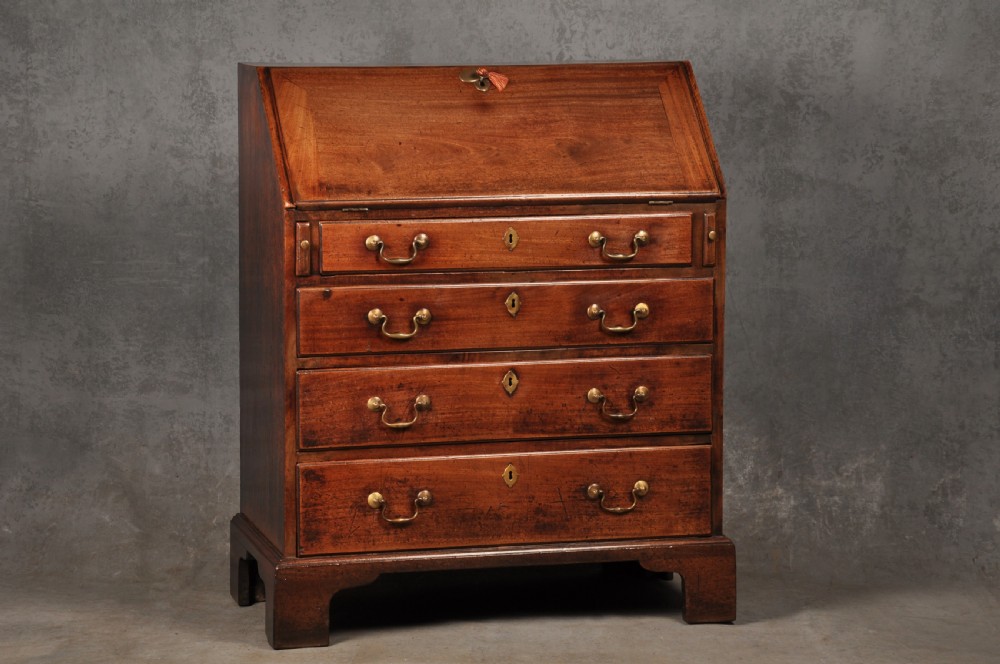 An 18th-century mahogany slant-front writing bureau featuring four graduated drawers with brass handles, standing on bracket feet.