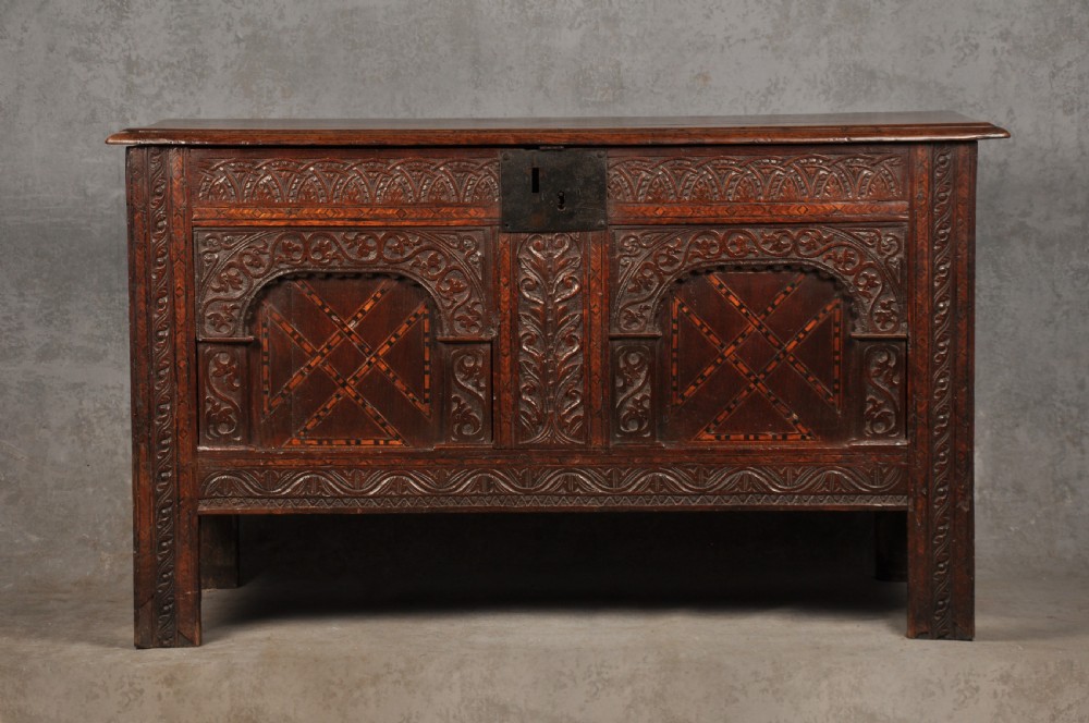 Early 17th-century dark carved oak coffer featuring dual arched panels with geometric inlay and an iron lock plate.