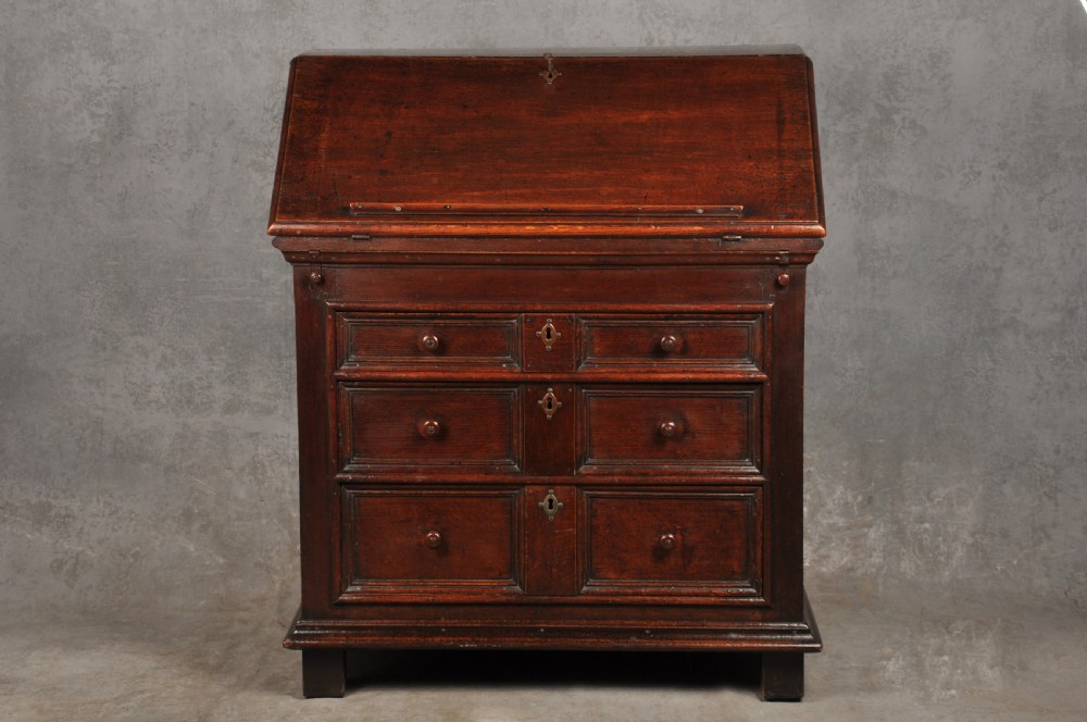 A 17th-century dark oak bureau featuring a sloped drop-down lid, geometric moulded drawers, and iron keyhole escutcheons.