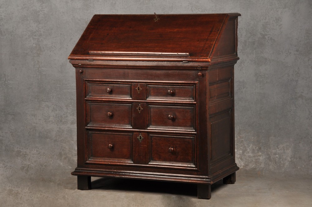 A 17th-century dark oak bureau featuring a sloped drop-down lid, geometric moulded drawers, and iron keyhole escutcheons. View II