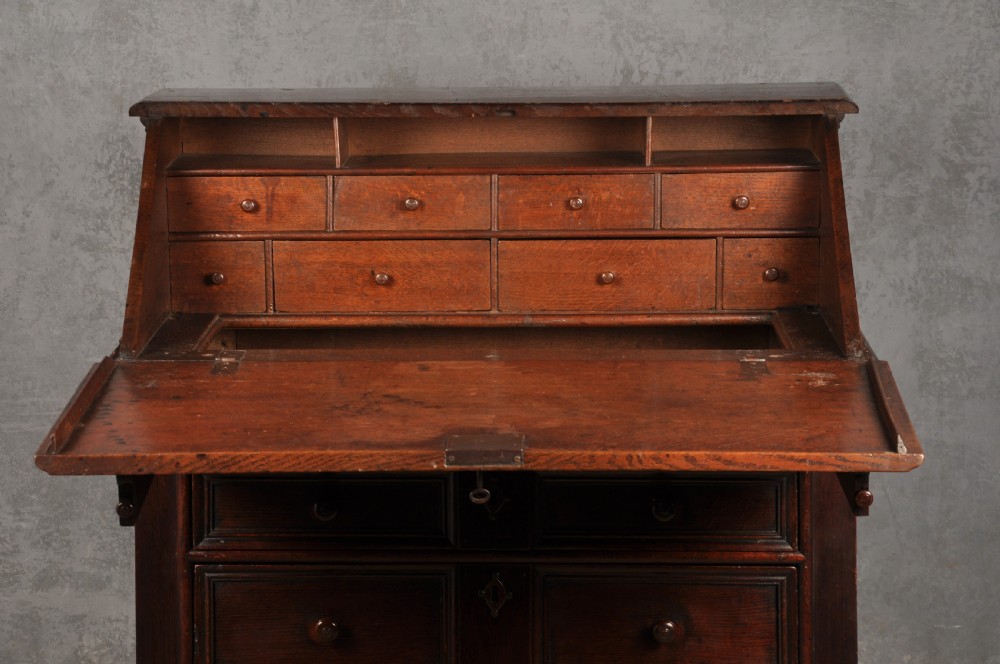 A 17th-century dark oak bureau featuring a sloped drop-down lid, geometric moulded drawers, and iron keyhole escutcheons. View IV