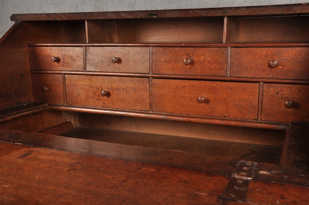 A 17th-century dark oak bureau featuring a sloped drop-down lid, geometric moulded drawers, and iron keyhole escutcheons. View V