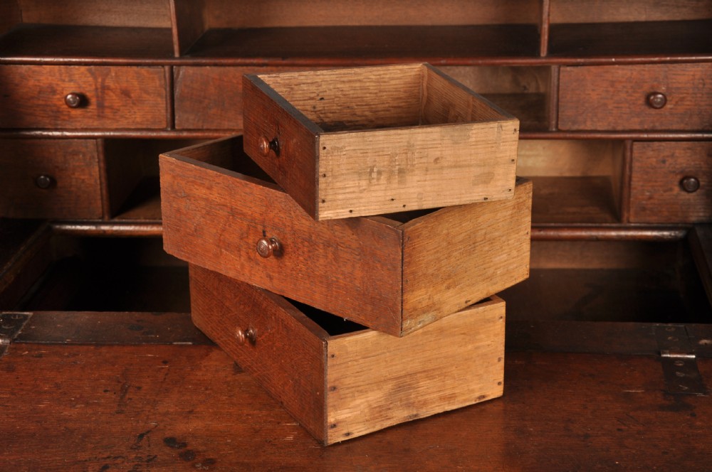 A 17th-century dark oak bureau featuring a sloped drop-down lid, geometric moulded drawers, and iron keyhole escutcheons. View VI