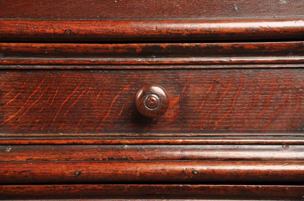 A 17th-century dark oak bureau featuring a sloped drop-down lid, geometric moulded drawers, and iron keyhole escutcheons. View X