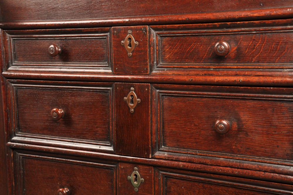 A 17th-century dark oak bureau featuring a sloped drop-down lid, geometric moulded drawers, and iron keyhole escutcheons. View XI