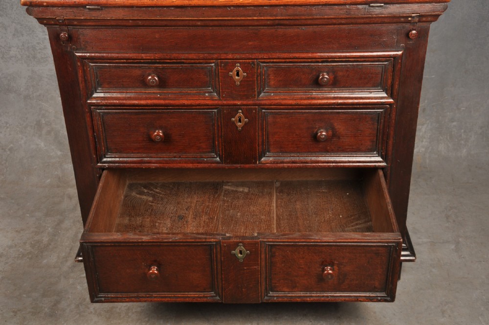 A 17th-century dark oak bureau featuring a sloped drop-down lid, geometric moulded drawers, and iron keyhole escutcheons. View XIV