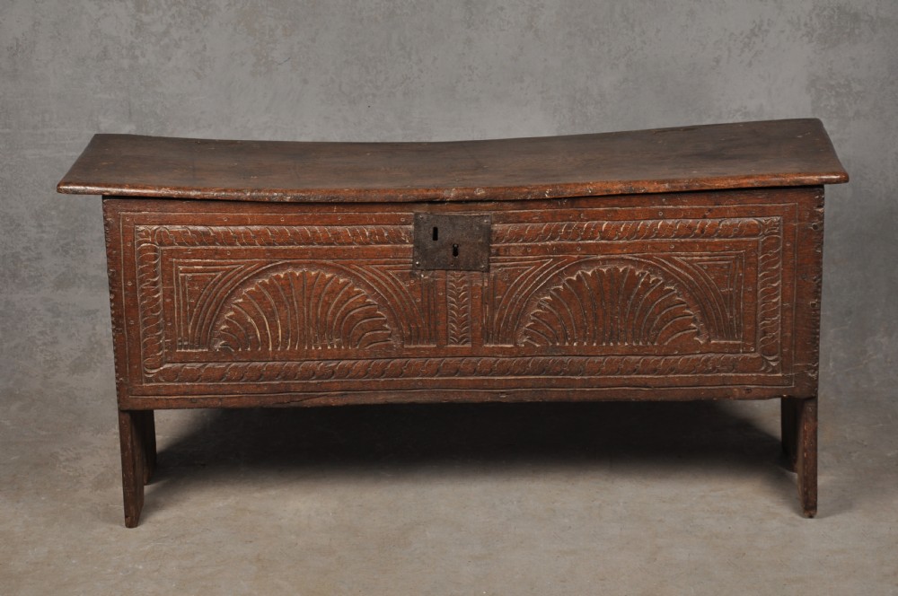 A low 17th-century dark oak coffer with relief carved lunette patterns and a central iron lockplate.