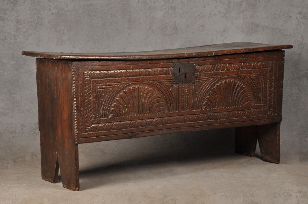 A low 17th-century dark oak coffer with relief carved lunette patterns and a central iron lockplate. View II
