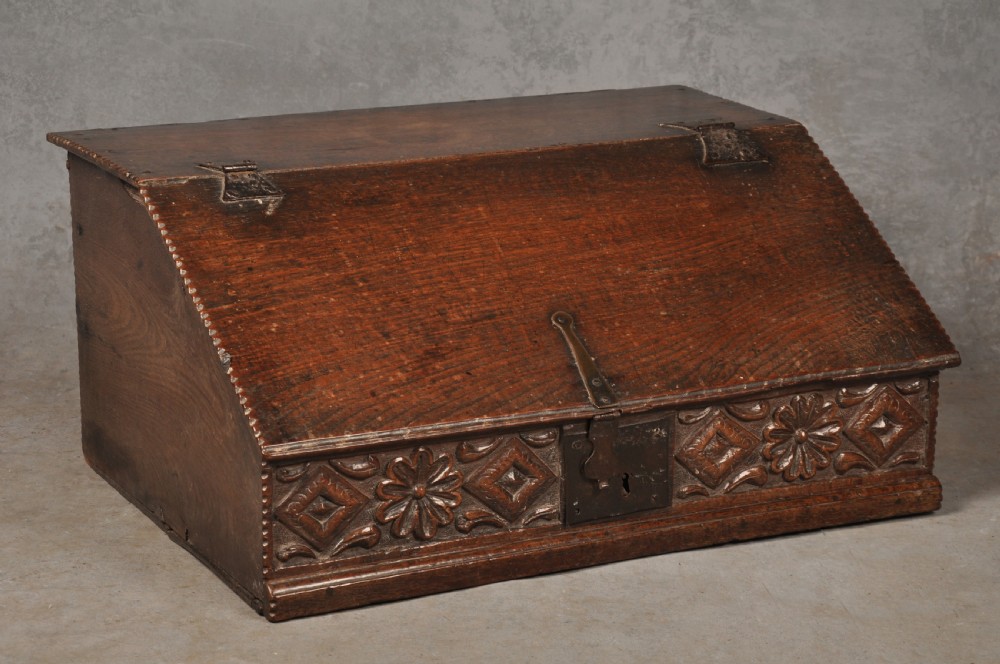 A seventeenth-century dark oak slant-front desk box with relief rosette carvings and iron hardware.