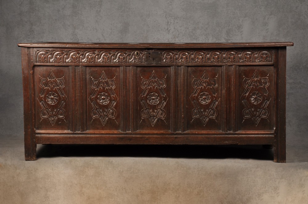 A large seventeenth-century dark oak coffer featuring five carved panels decorated with geometric lozenge and rosette motifs beneath a carved upper frieze.