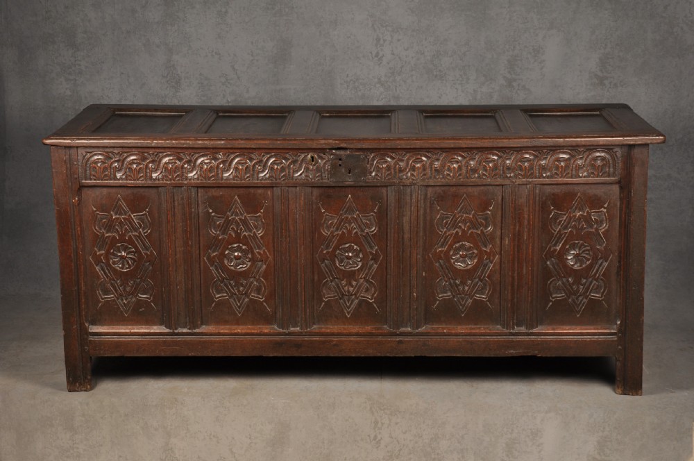 A large seventeenth-century dark oak coffer featuring five carved panels decorated with geometric lozenge and rosette motifs beneath a carved upper frieze. View II