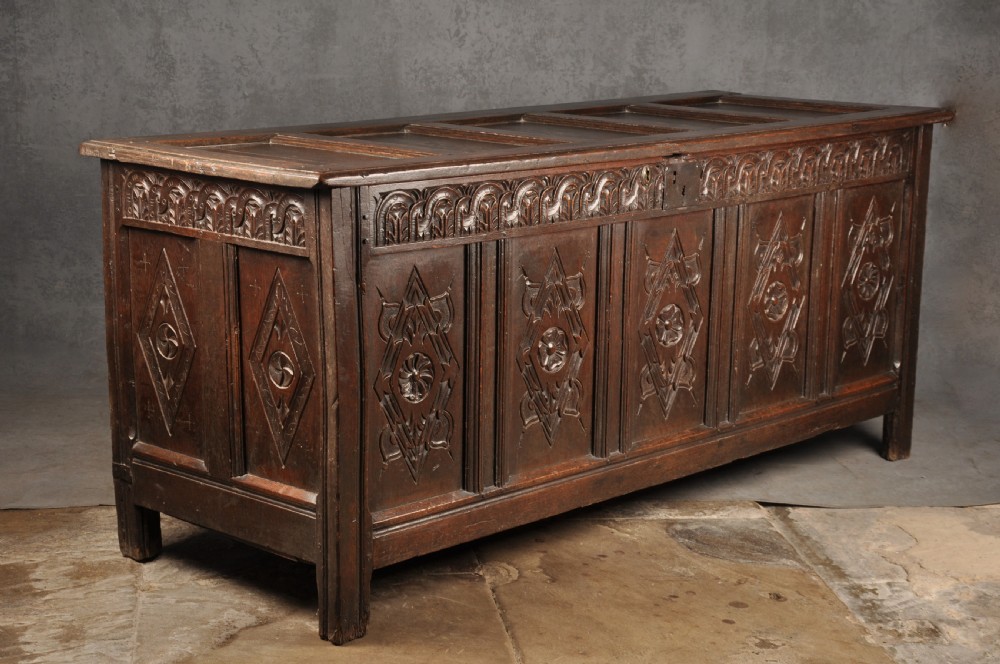 A large seventeenth-century dark oak coffer featuring five carved panels decorated with geometric lozenge and rosette motifs beneath a carved upper frieze. View III