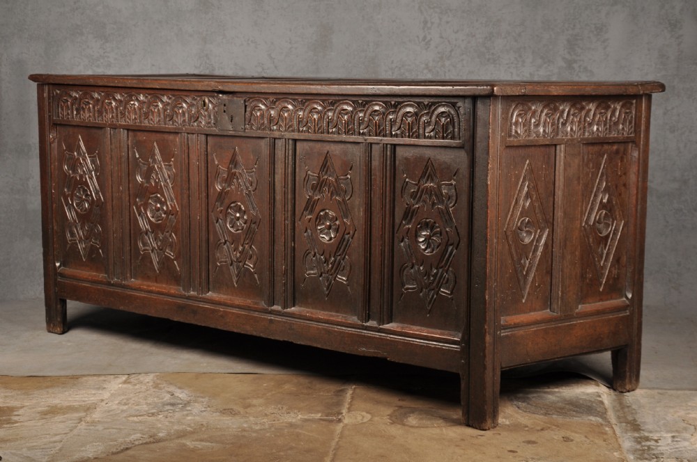 A large seventeenth-century dark oak coffer featuring five carved panels decorated with geometric lozenge and rosette motifs beneath a carved upper frieze. View IV