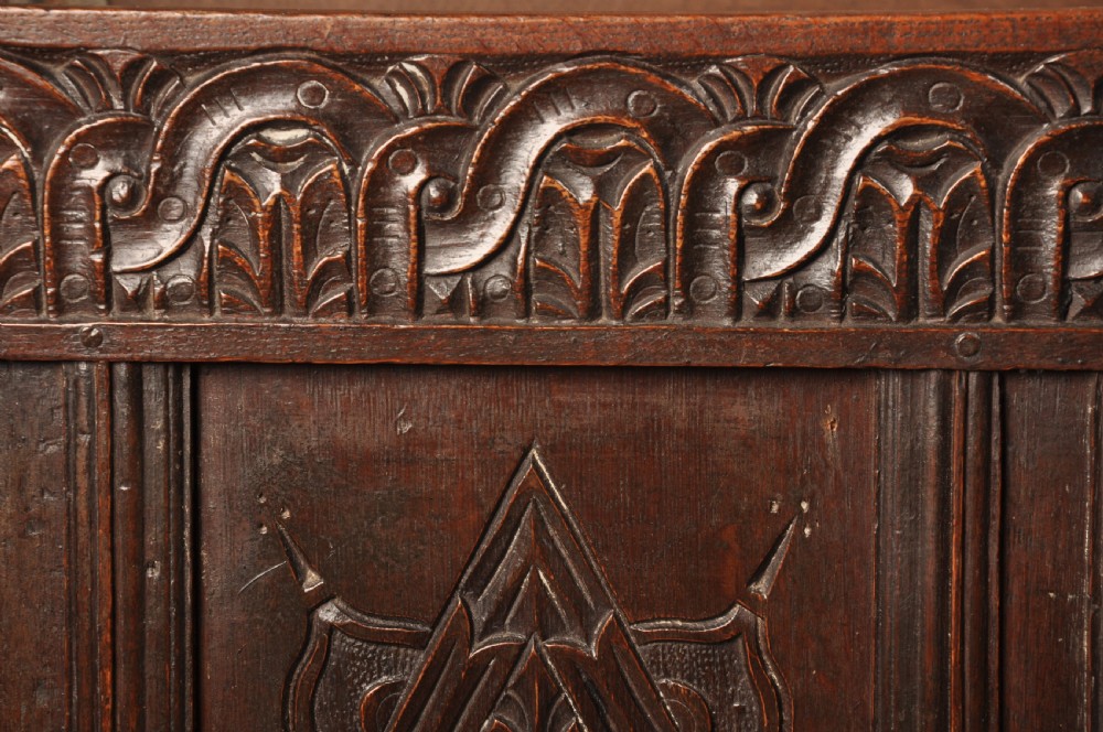 A large seventeenth-century dark oak coffer featuring five carved panels decorated with geometric lozenge and rosette motifs beneath a carved upper frieze. View VIII