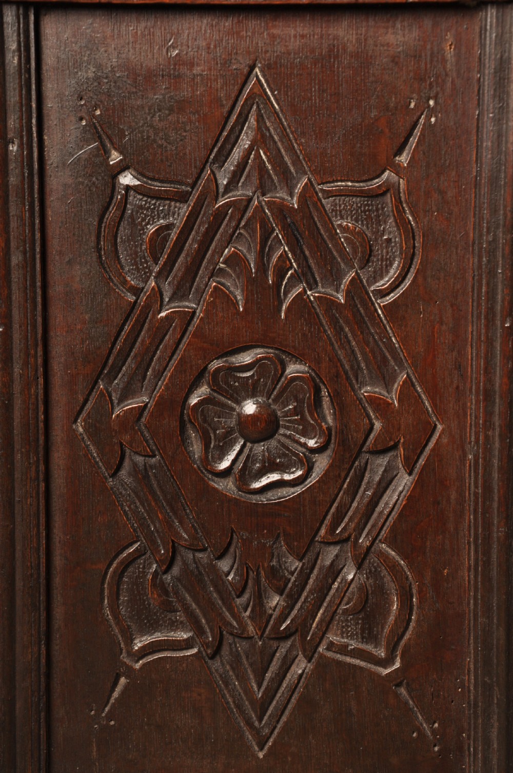 A large seventeenth-century dark oak coffer featuring five carved panels decorated with geometric lozenge and rosette motifs beneath a carved upper frieze. View IX