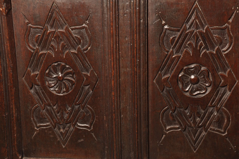 A large seventeenth-century dark oak coffer featuring five carved panels decorated with geometric lozenge and rosette motifs beneath a carved upper frieze. View X