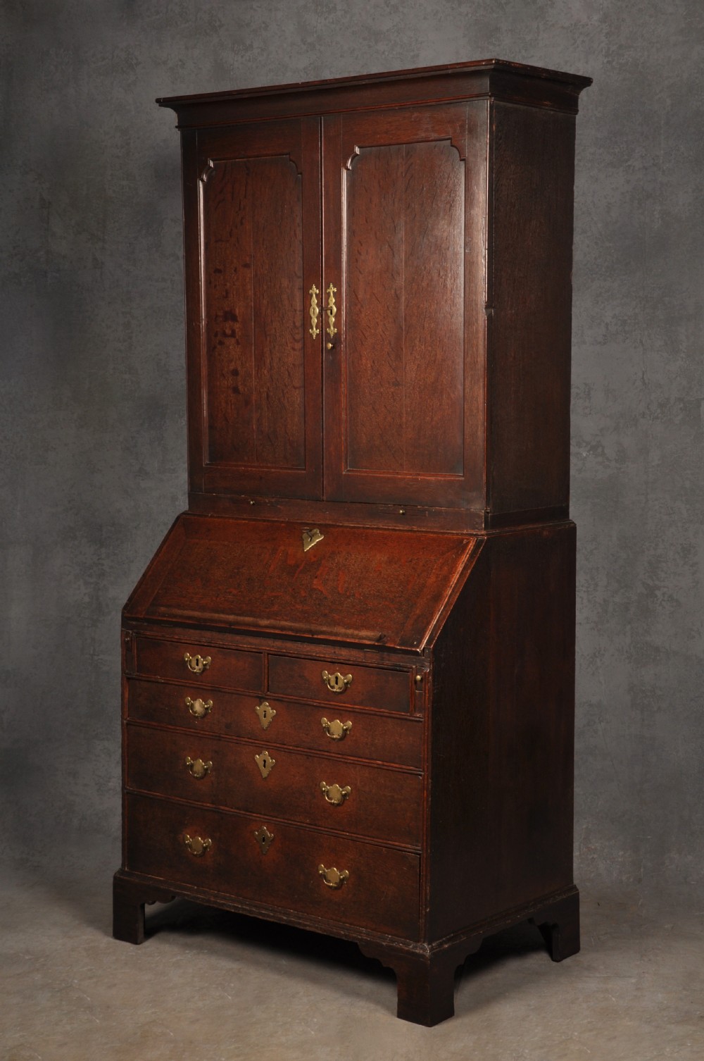 An early 18th-century dark oak bureau bookcase with a two-door upper section, a sloped writing fall, and long drawers on bracket feet.