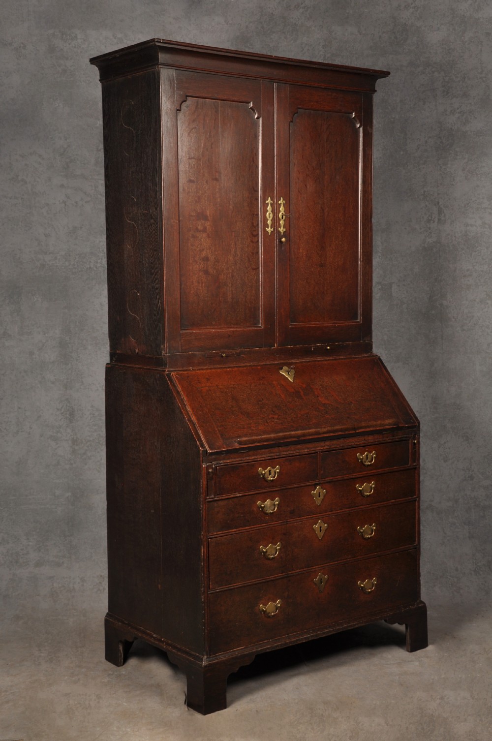 An early 18th-century dark oak bureau bookcase with a two-door upper section, a sloped writing fall, and long drawers on bracket feet. View II