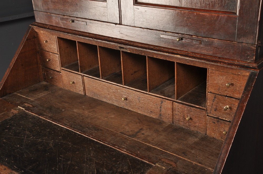 An early 18th-century dark oak bureau bookcase with a two-door upper section, a sloped writing fall, and long drawers on bracket feet. View V