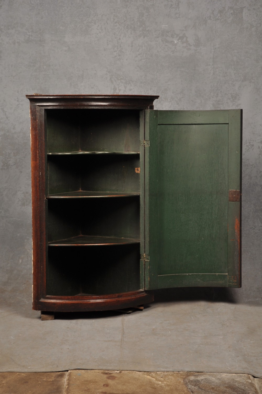 An early eighteenth-century dark oak bow-fronted corner cupboard featuring a curved fielded panel door, brass escutcheon, and moulded cornice. View III