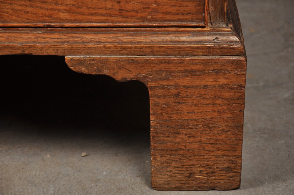 An 18th-century Georgian oak chest of drawers featuring two short drawers over three long drawers with brass drop handles and bracket feet. View V