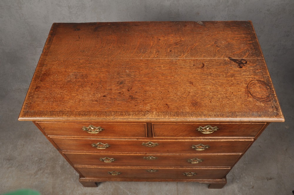 An 18th-century Georgian oak chest of drawers featuring two short drawers over three long drawers with brass drop handles and bracket feet. View VI