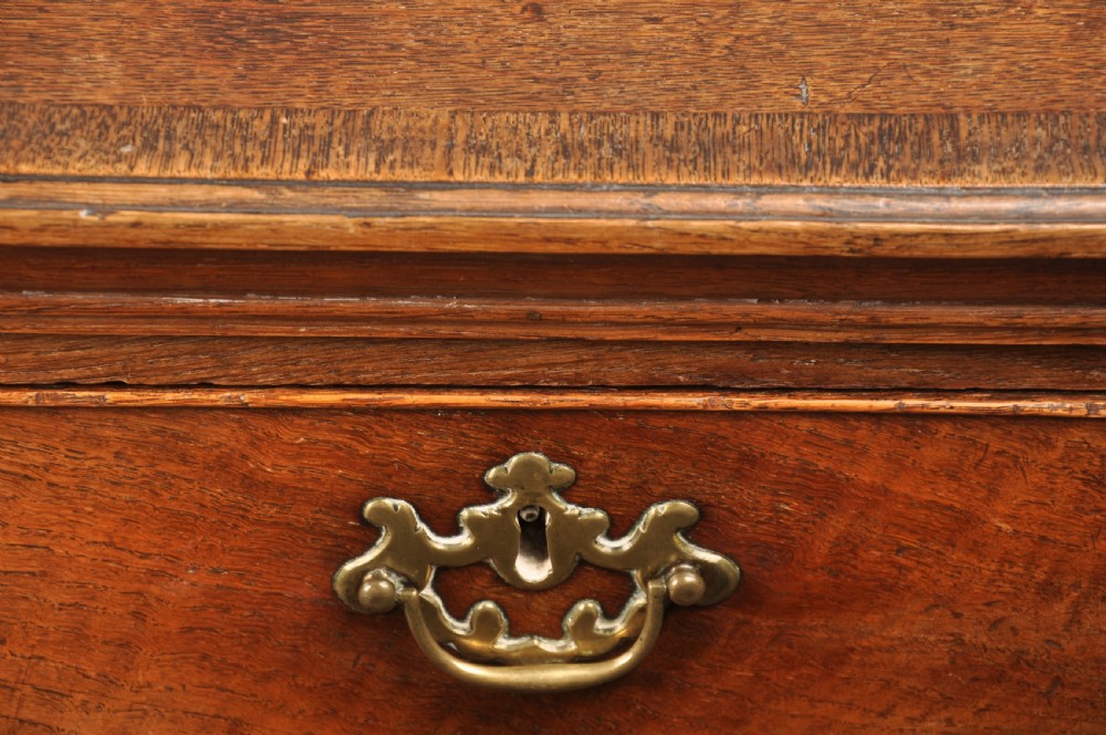 An 18th-century Georgian oak chest of drawers featuring two short drawers over three long drawers with brass drop handles and bracket feet. View XII