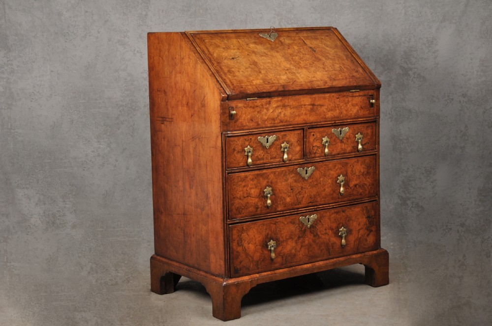 An early eighteenth-century burr walnut bureau featuring a sloped fall-front writing flap above four graduated drawers with brass drop handles and bracket feet. View XIV