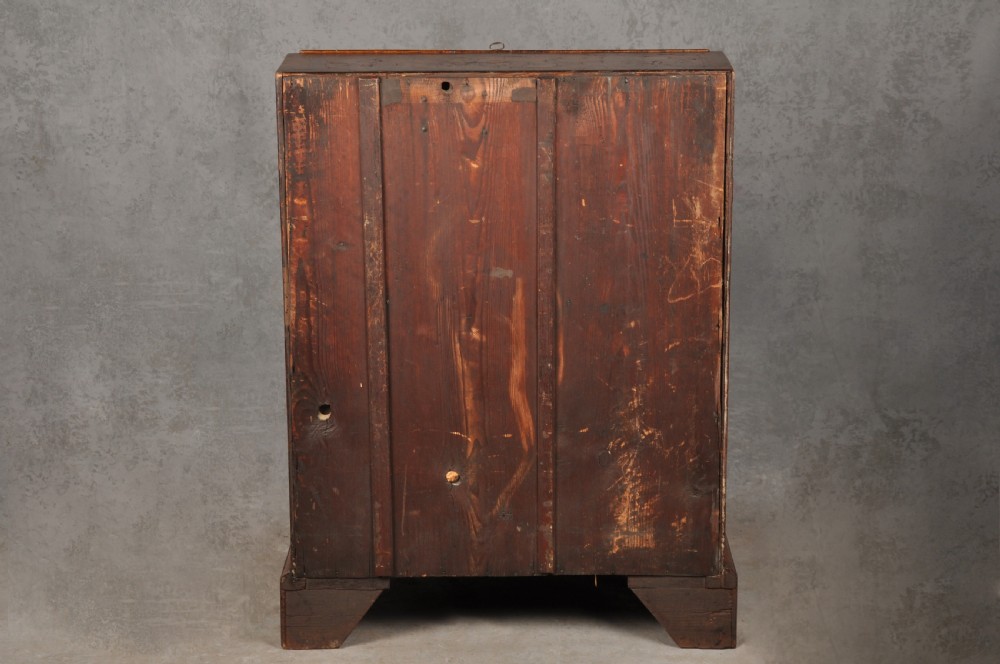 An early eighteenth-century burr walnut bureau featuring a sloped fall-front writing flap above four graduated drawers with brass drop handles and bracket feet. View XV