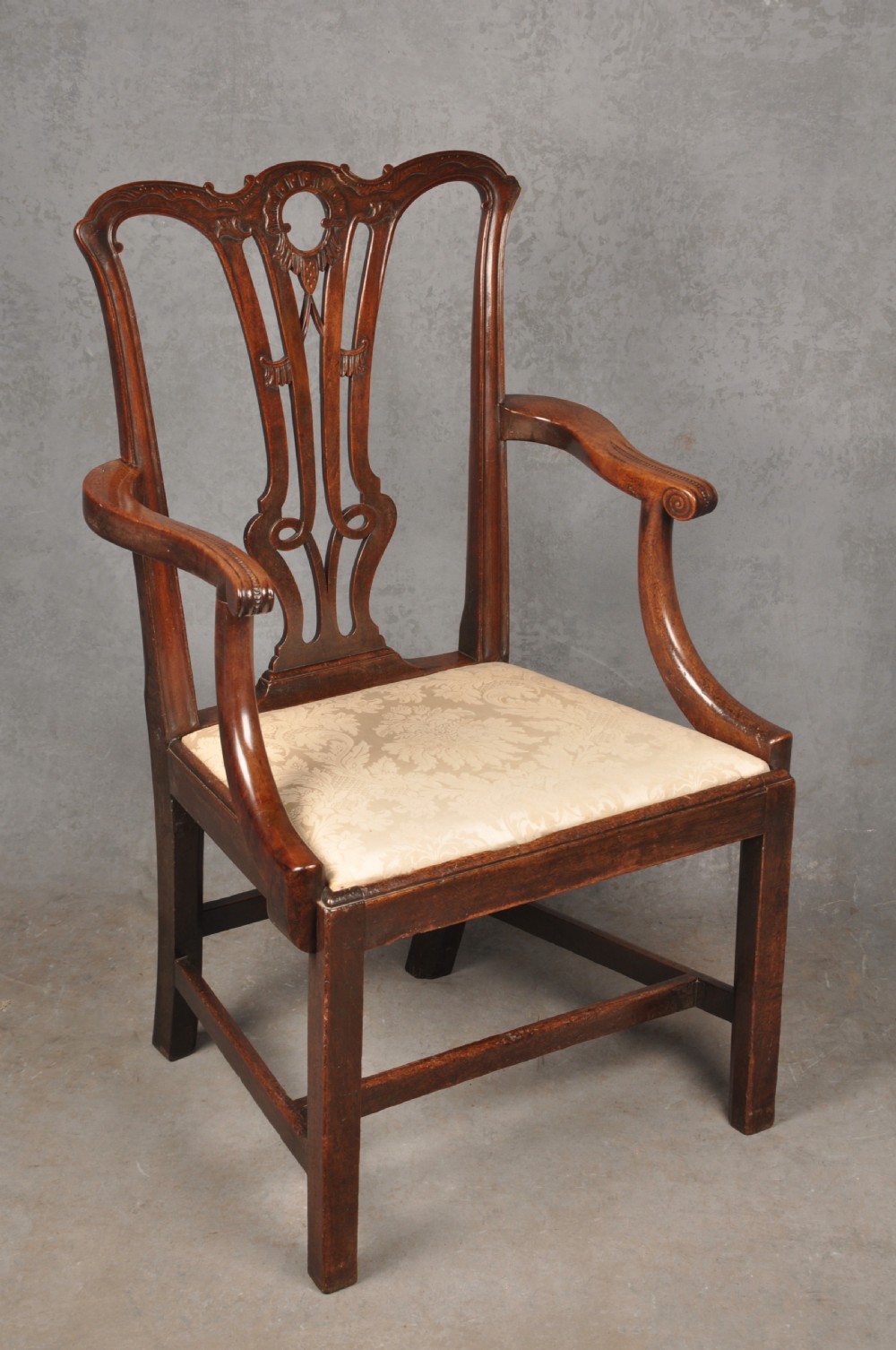 An 18th-century Chippendale mahogany armchair with a carved pierced back splat, curved arms, and a cream upholstered seat.