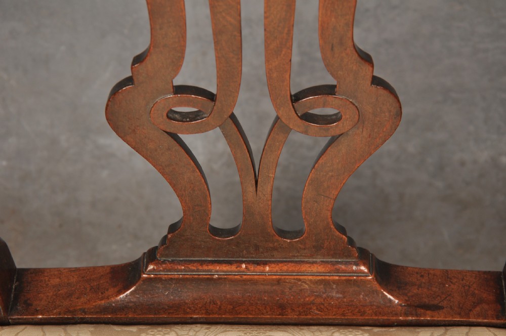 An 18th-century Chippendale mahogany armchair with a carved pierced back splat, curved arms, and a cream upholstered seat. View V