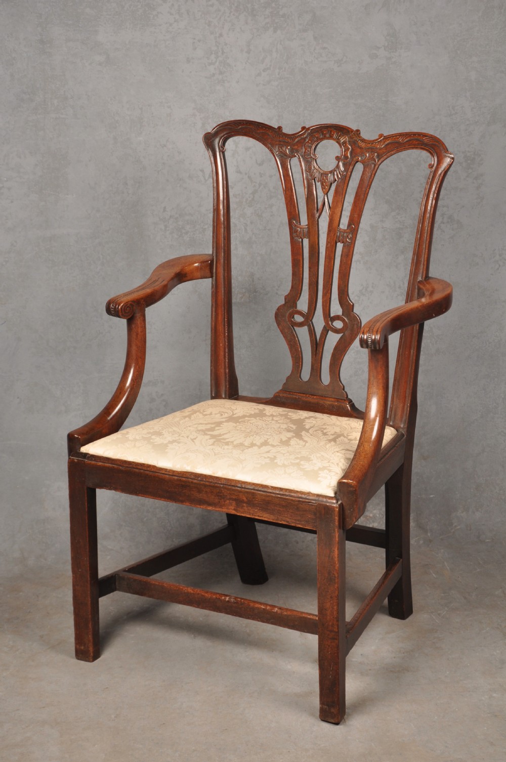 An 18th-century Chippendale mahogany armchair with a carved pierced back splat, curved arms, and a cream upholstered seat. View X