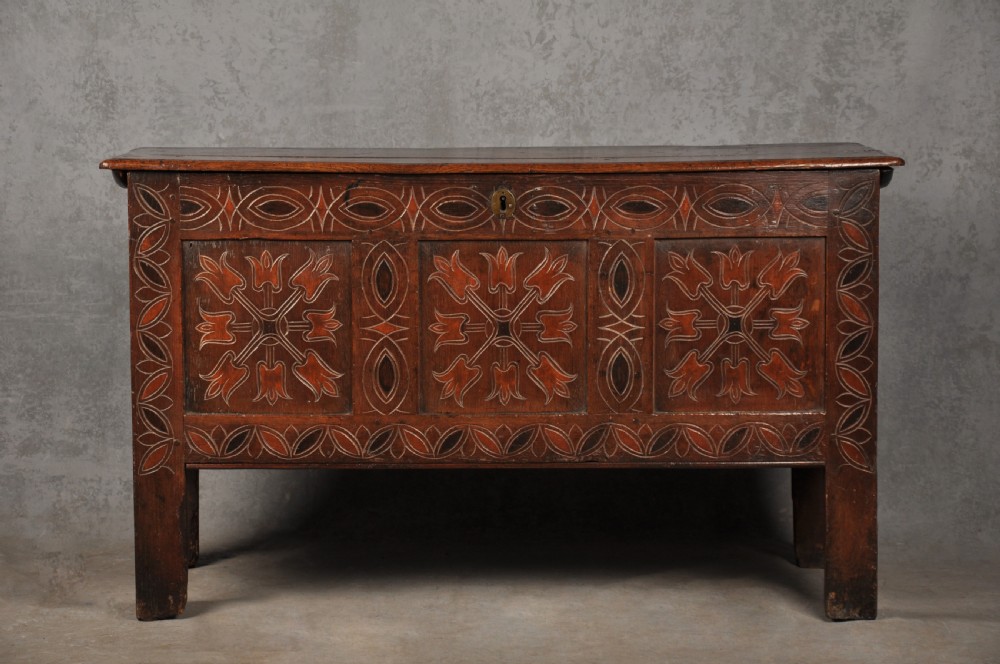 A 17th-century dark stained oak coffer with carved tulip panels and geometric border details.