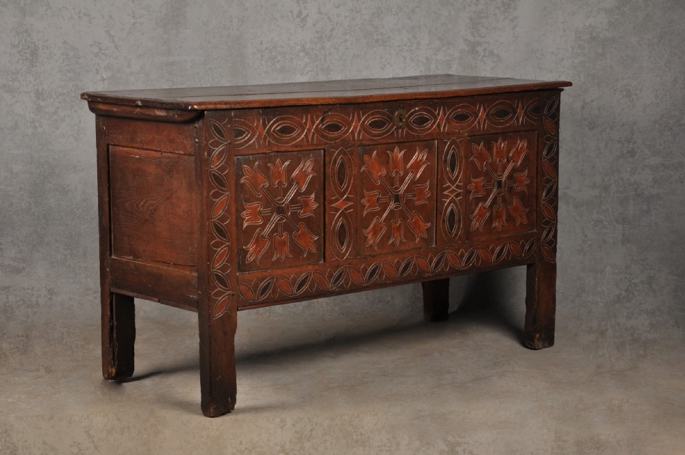 A 17th-century dark stained oak coffer with carved tulip panels and geometric border details. View II