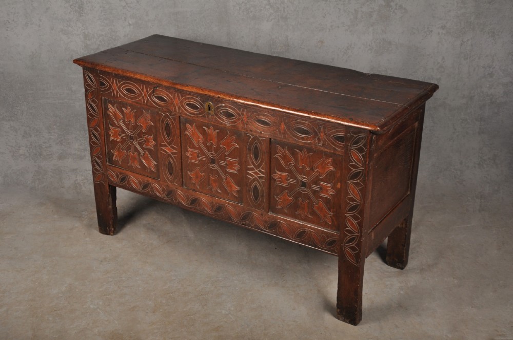 A 17th-century dark stained oak coffer with carved tulip panels and geometric border details. View III